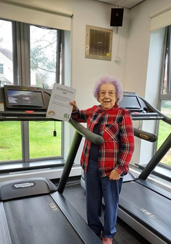Service user Olive holding her sponsorship poster by a treadmill