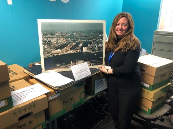 Annette Mackin, Heritage Officers of Archives holding a photo showing Canary Wharf London Docklands pre-development