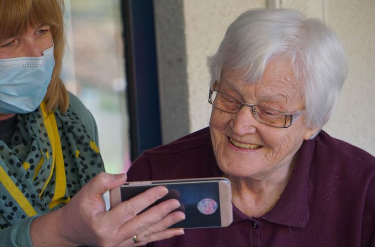 Carer in mask shares image on her phone with elderly lady