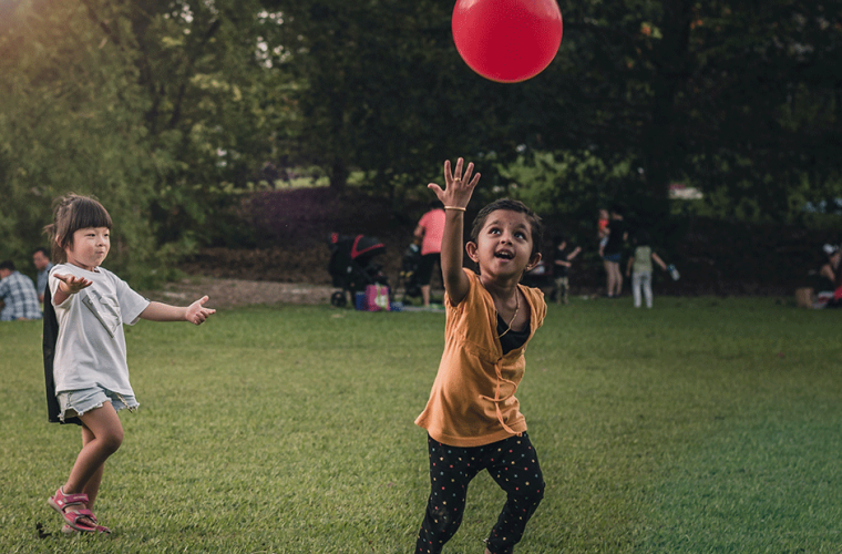 two children running to get a red balloon in a park 