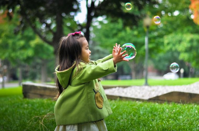 young girl in green coat holding bubbles