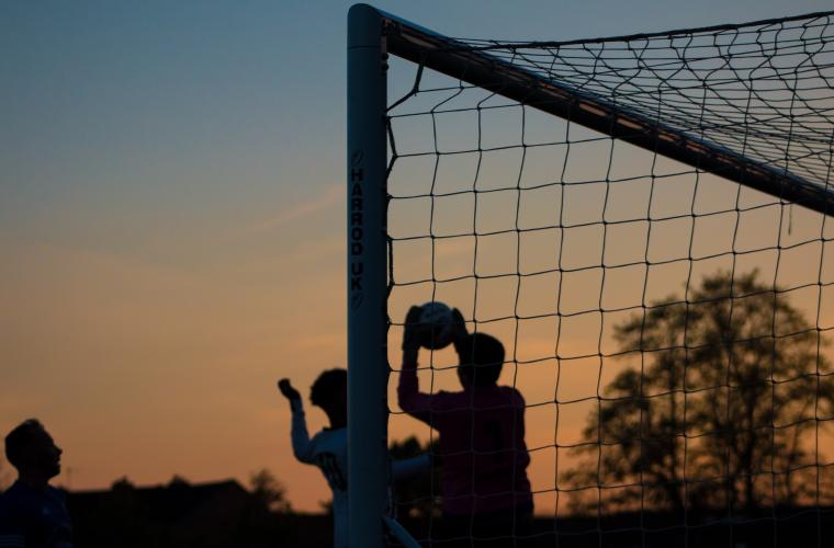 Person in goal catching a football whilst the sun sets. 
