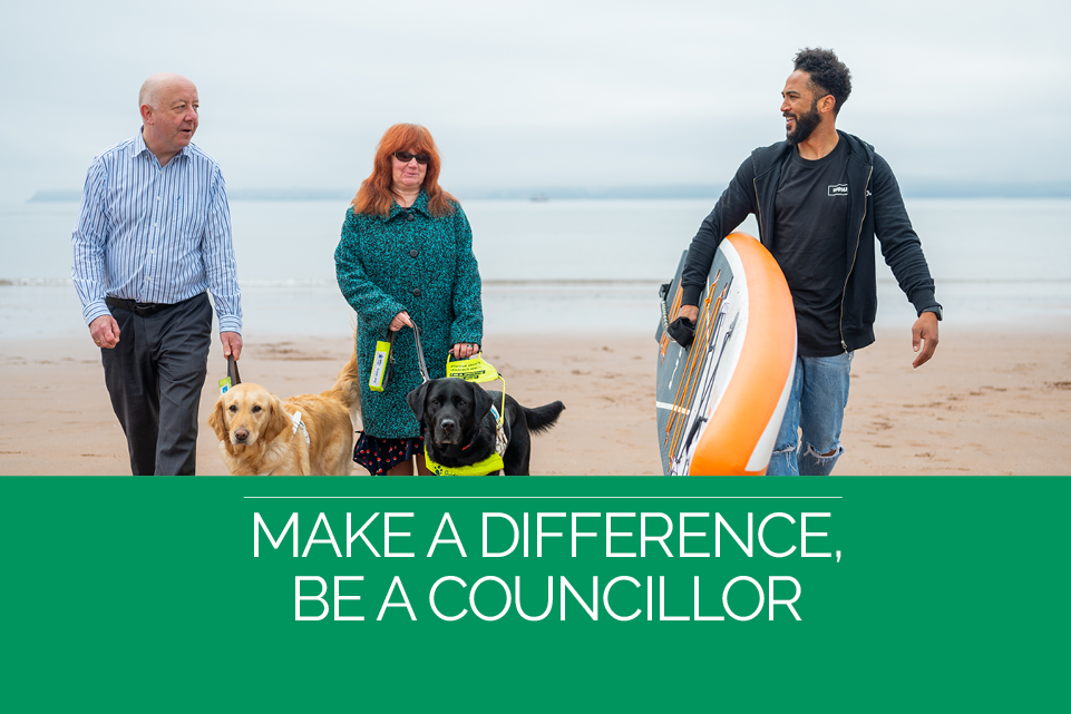 Three people on the beach with two dogs and a surfboard