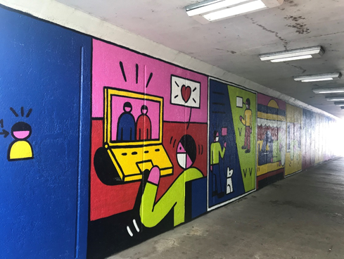 A graffiti underground wall with a graphic person wearing a facemask and talking over a computer