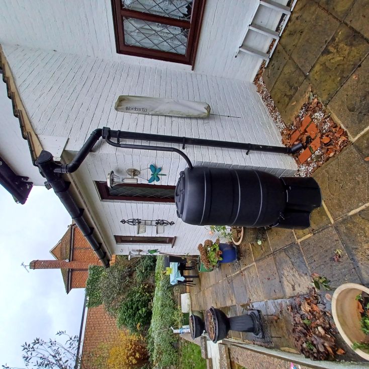 Black water butt installed against white outside wall of a house