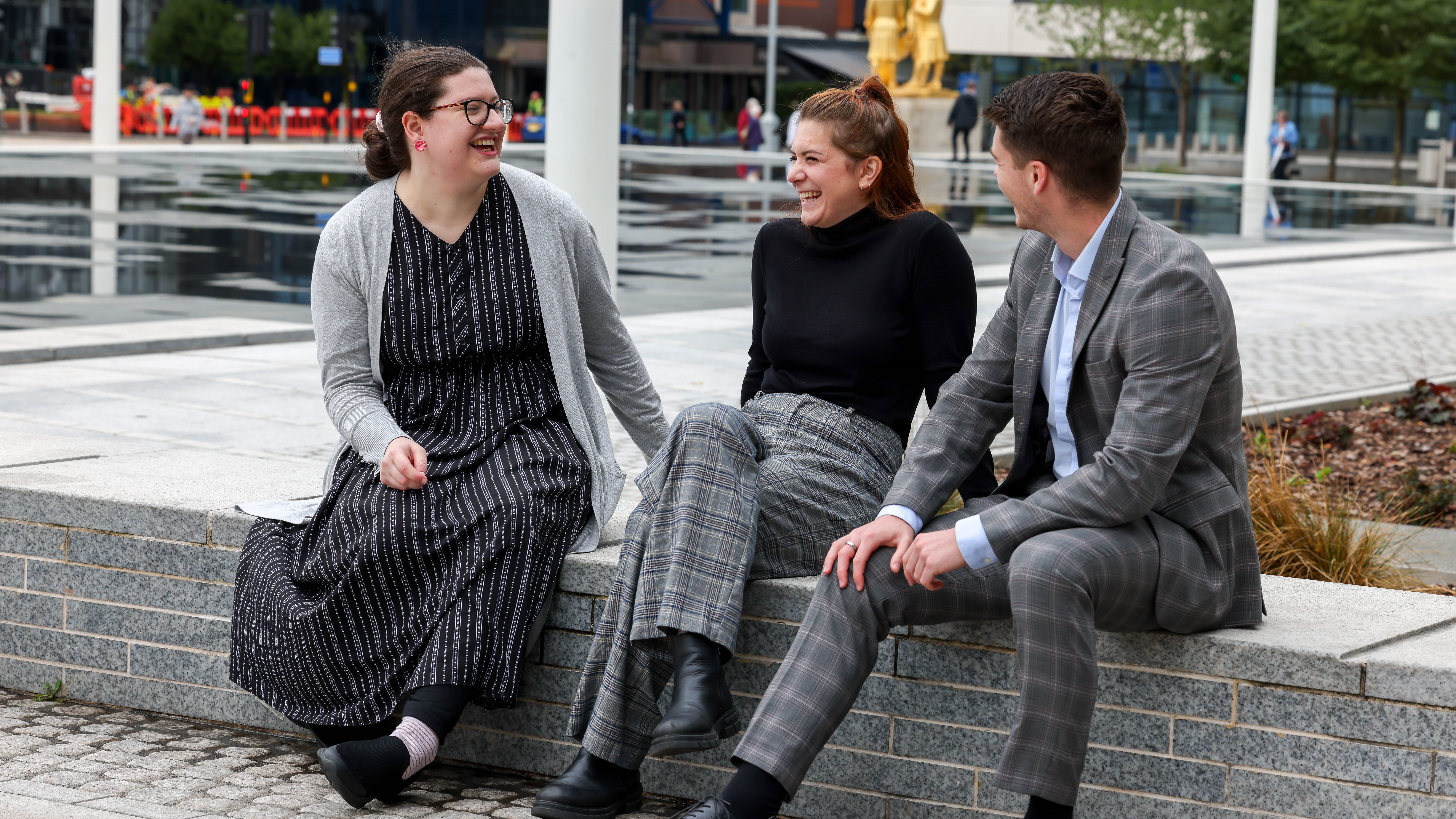 Three NGDP graduates sitting on wall outside dressed in work attire