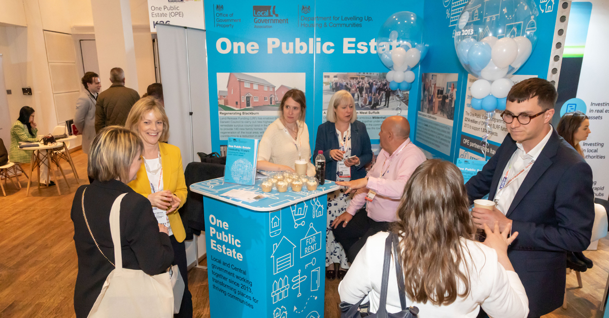 A group of delegates and staff talking at One Public Estate's stand at UKFEiiF 2023