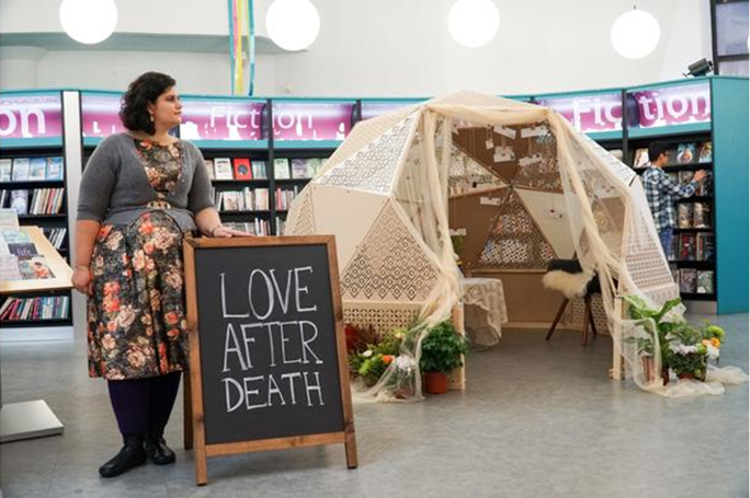 A lady standing next to a sign saying 'Love after death' in a library