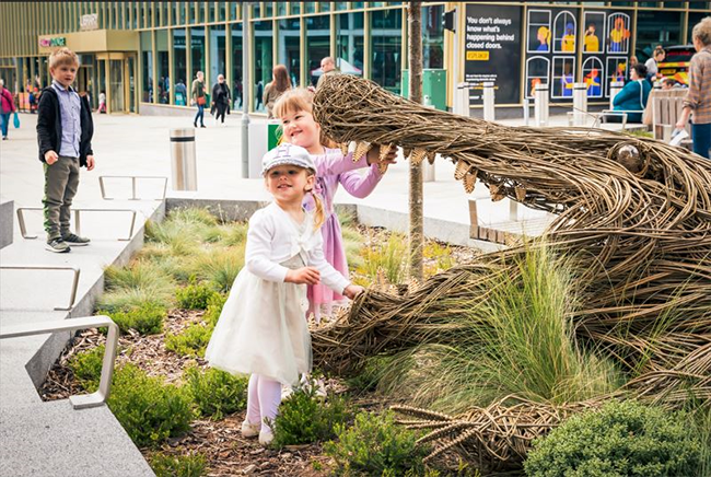 Two children stood next to a crocodile willow sculpture in Barnsley’s transformed town centre. The willow sculpture is part of ‘Twisted’, Barnsley’s annual natural art festival. 