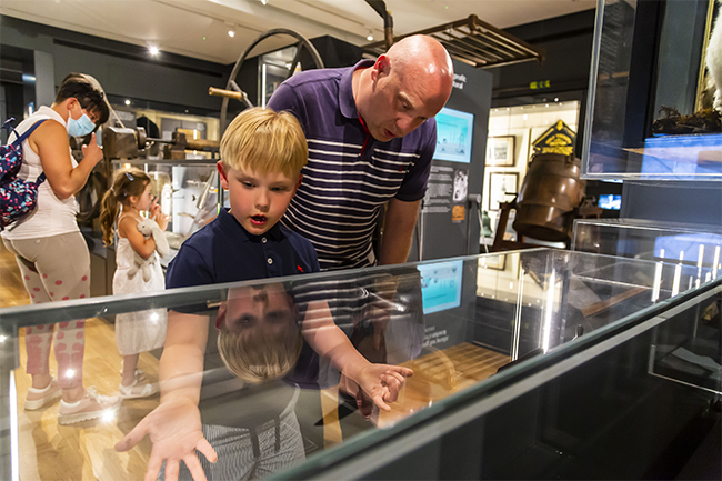 Visitors to Craven Museum. A man and a boy are looking in wonder into a glass case and behind them, a woman and a young girl are looking at a different display.  