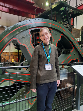 Daniel, a volunteer at Sheffield Museums, is standing in front of the giant fly wheel of the River Don Engine at Kelham Island Museum. 