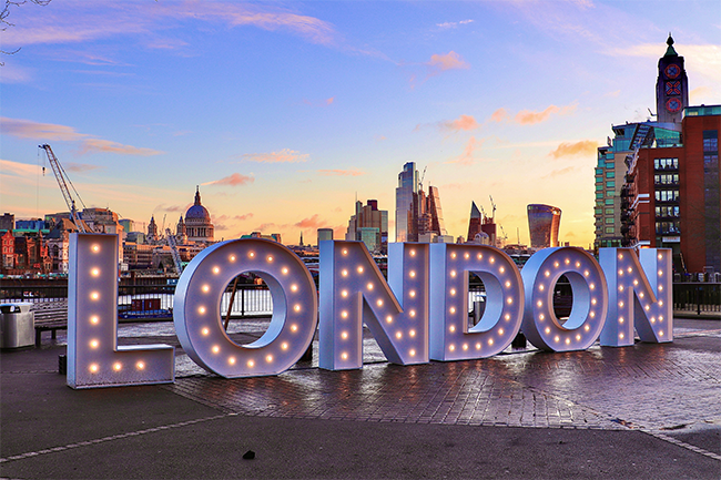 A large lit up sign of the word 'London' by the river Thames