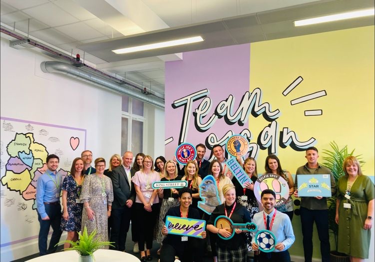 The ten LG Challenge contestants posing for a photo with Wigan Council colleagues, holding a variety of photo props
