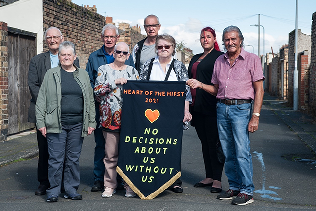 A group of people standing outside with a banner that reads 'Heart of Hirst 2021, No decisions about us without us'