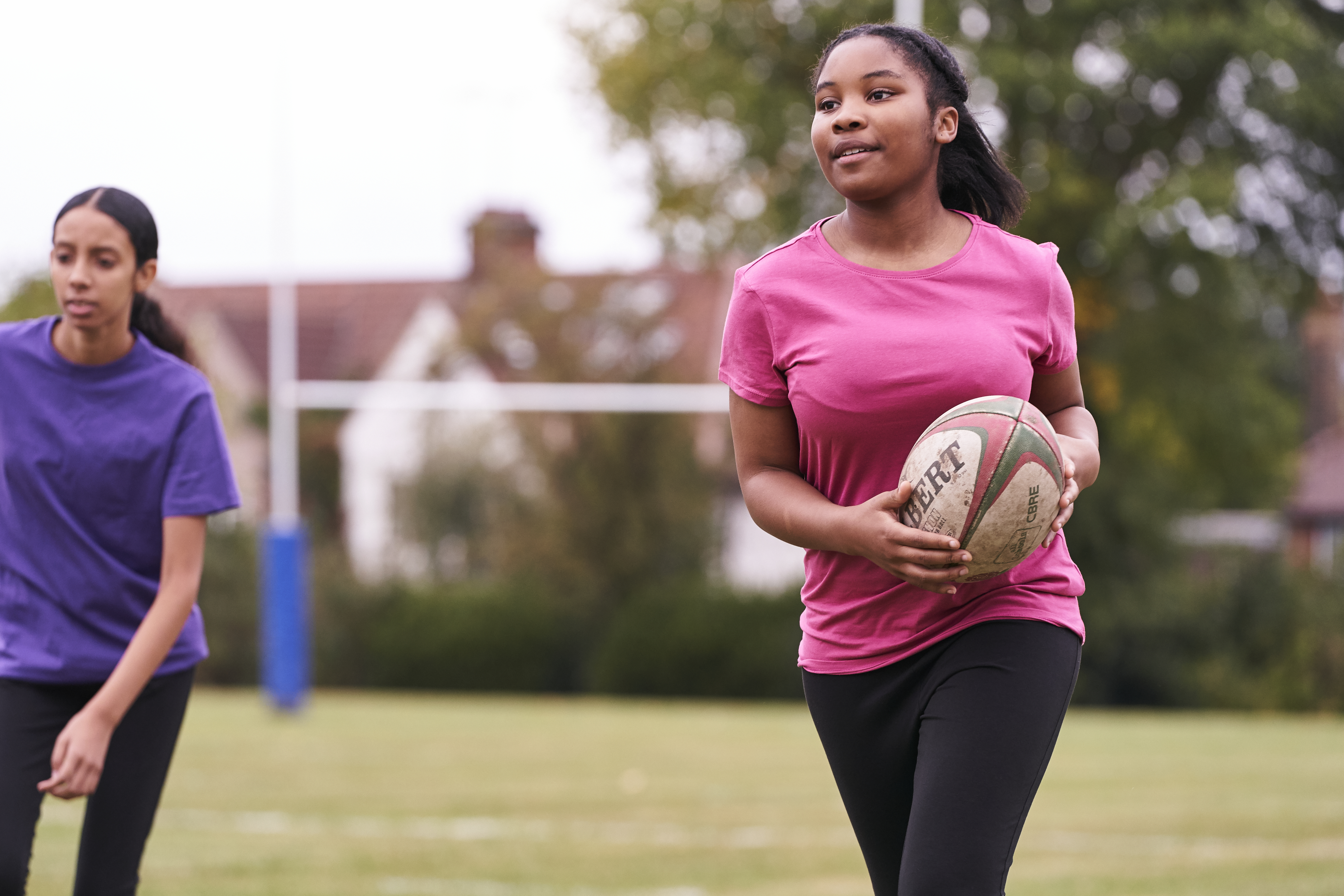 A young girl playing rugby on a field, holding the rugby ball
