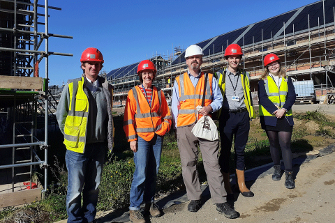 five people wearing protective gear posing in front of a construction site