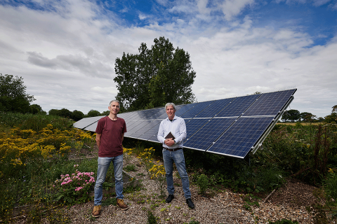 2 men posing in front of a big solar panel