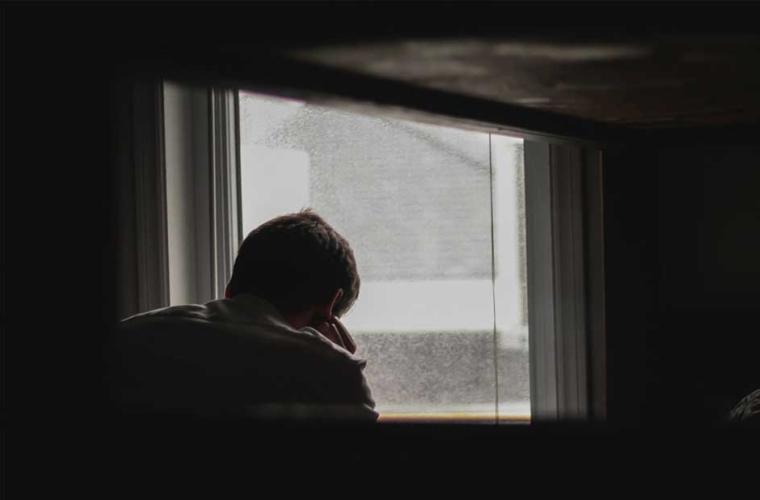 Man sitting in a dark room facing a window