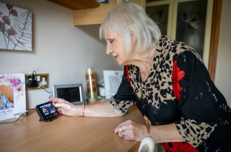 Older woman leaning on kitchen table checking her smart meter