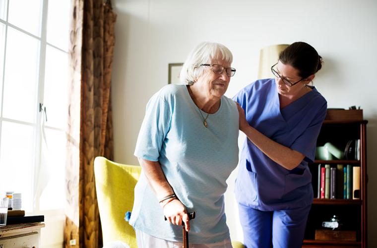 A home nurse aids an elderly woman to stand up and walk 