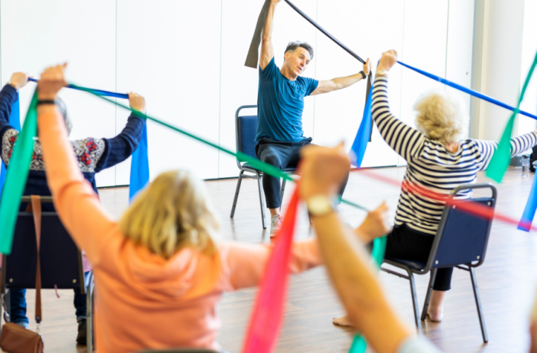 Exercise class, with people sat on chairs holding up elasticated bands 