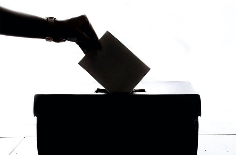 Silhouette of hand putting a vote in a ballot box