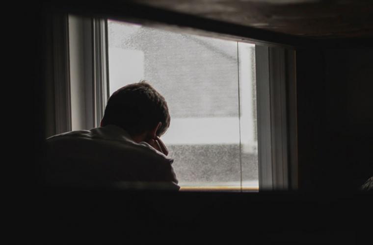 Young person looking out of a window from a darkened room
