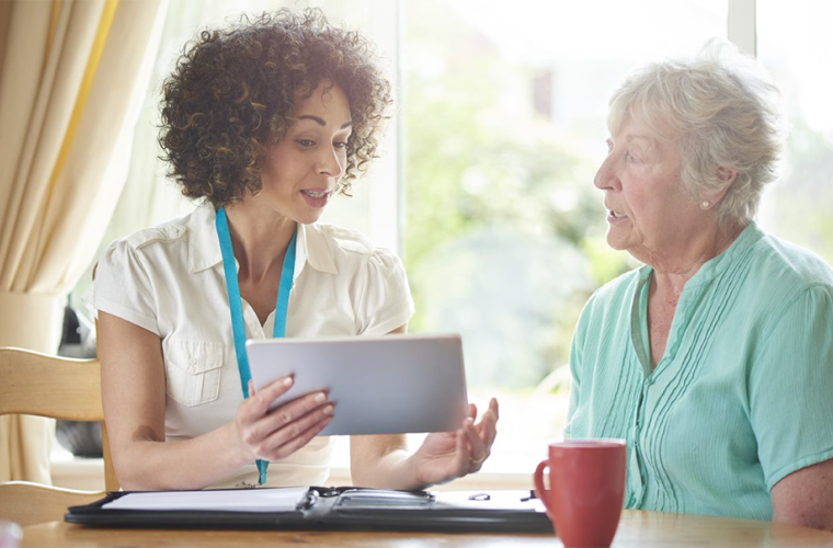 Younger woman carer showing older woman something on an iPad with a cup of tea