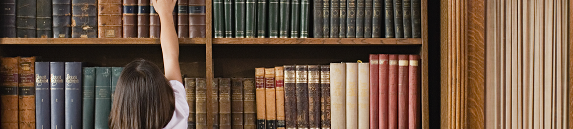 young girl trying to reach books in a tall library shelf
