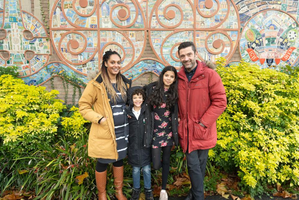 A mixed race family stand in front of a mural and yellow flowers