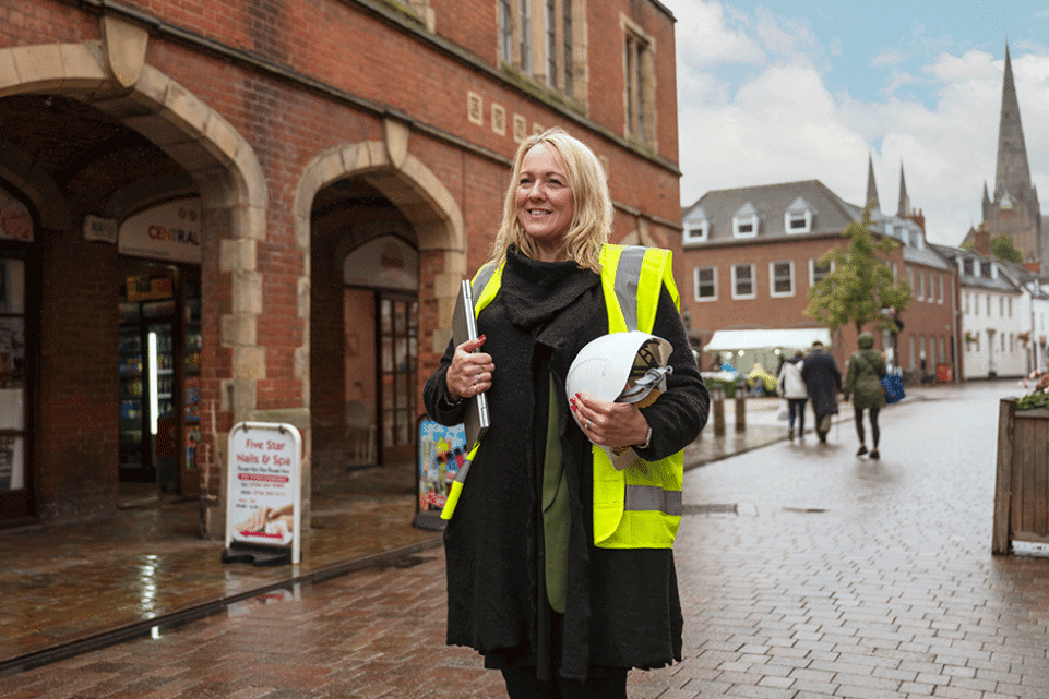 Female worker holding a construction helmet and wearing bright vest