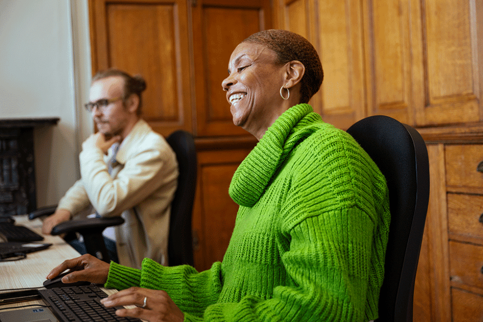 Female working behind on a desk. She is smiling looking to the computer