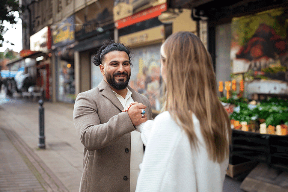 A young man shaking hands with a young woman on a street outside some shops