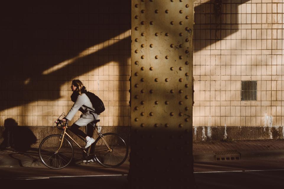 Lone woman cycling from the sunlight into the shadows.